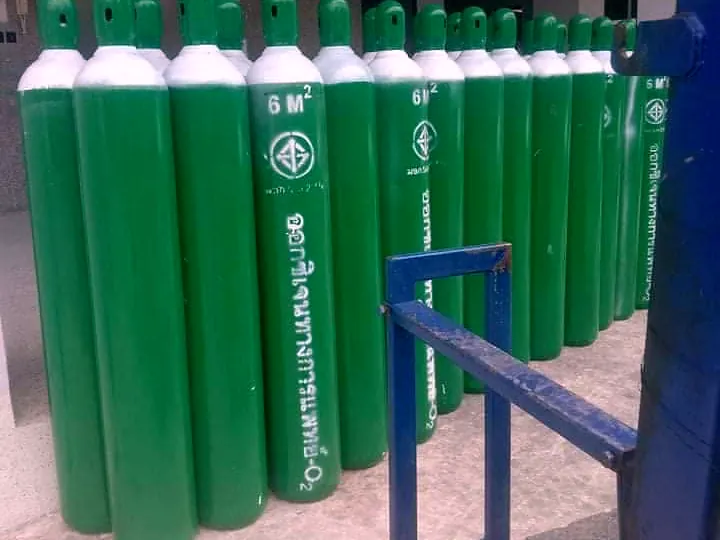 Rows of green oxygen cylinders in a storage area beside a blue steel rail