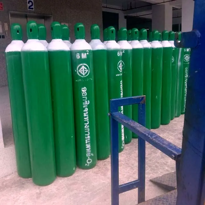 Rows of green oxygen cylinders in a storage area beside a blue steel rail